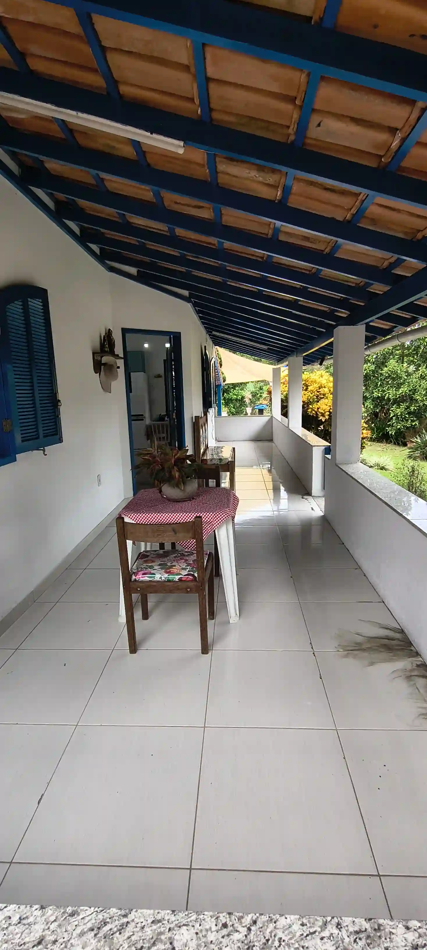 Vista vertical da varanda colonial com piso cerâmico claro, forro de madeira e estrutura pintada de azul